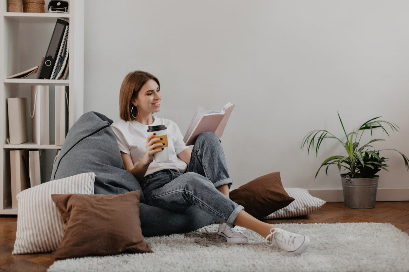 Woman smiling while reading a book in a floor-level reading corner.
