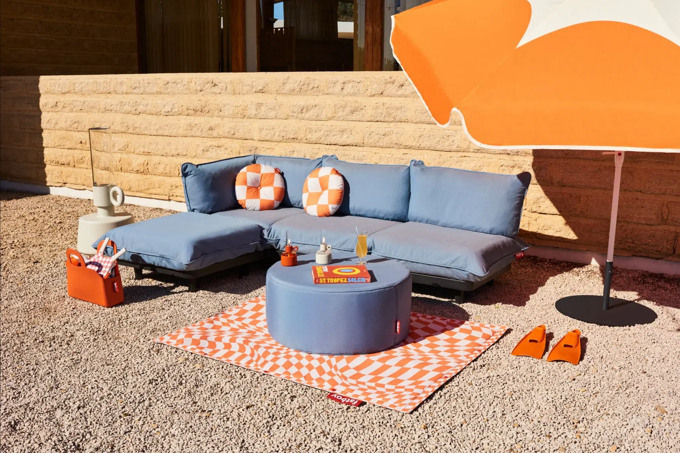 Modular balcony furniture set with blue cushions, round ottoman, and parasol, made with eco-friendly materials for a relaxed patio furniture setup.