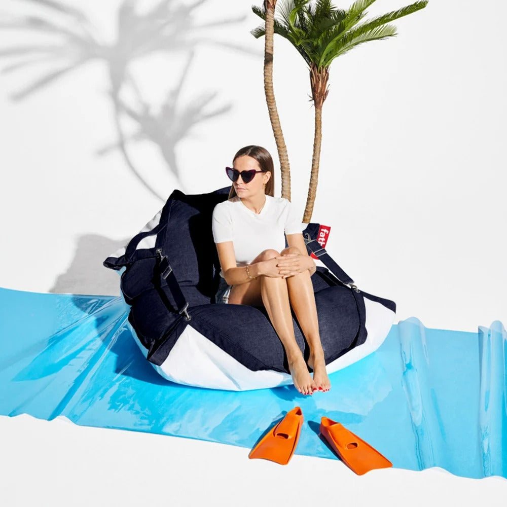 Woman sitting on a navy and white beanbag chair near a palm tree with swimming fins on a blue mat.