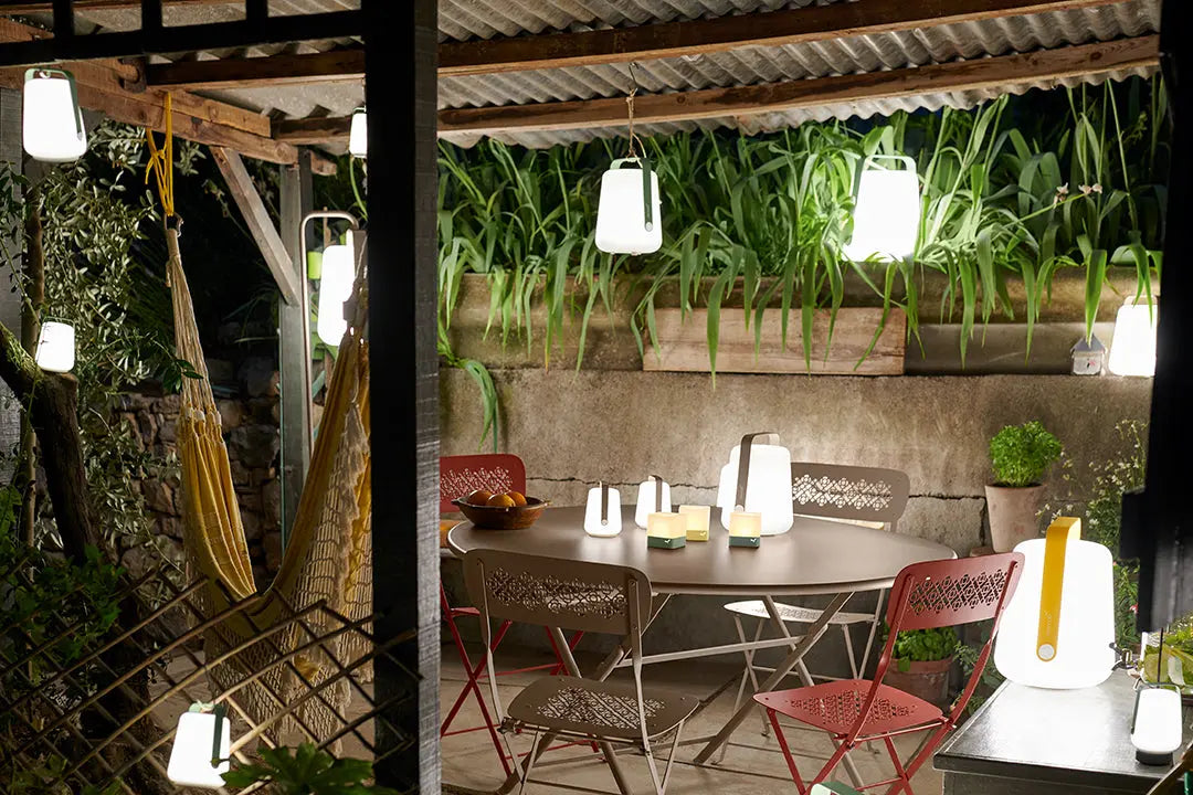 Layered outdoor lighting of Fermob Balad table lamps in a patio set.