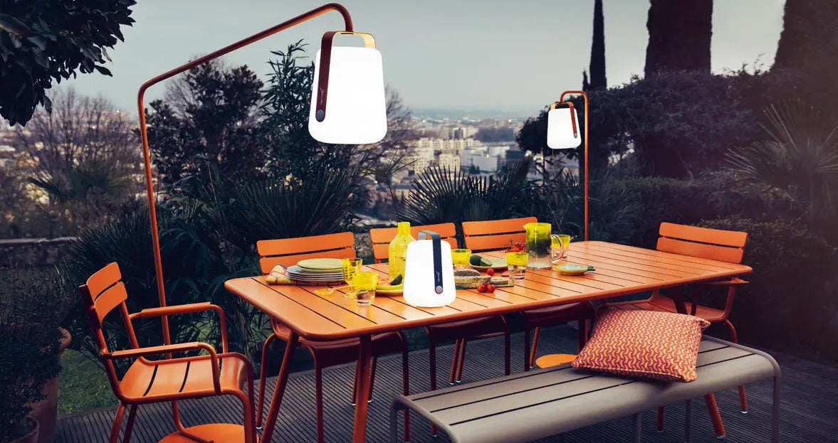 Fermob Balad table lamps and hanging lanterns with Fermob Louisiane table and armchairs on an outdoor patio.