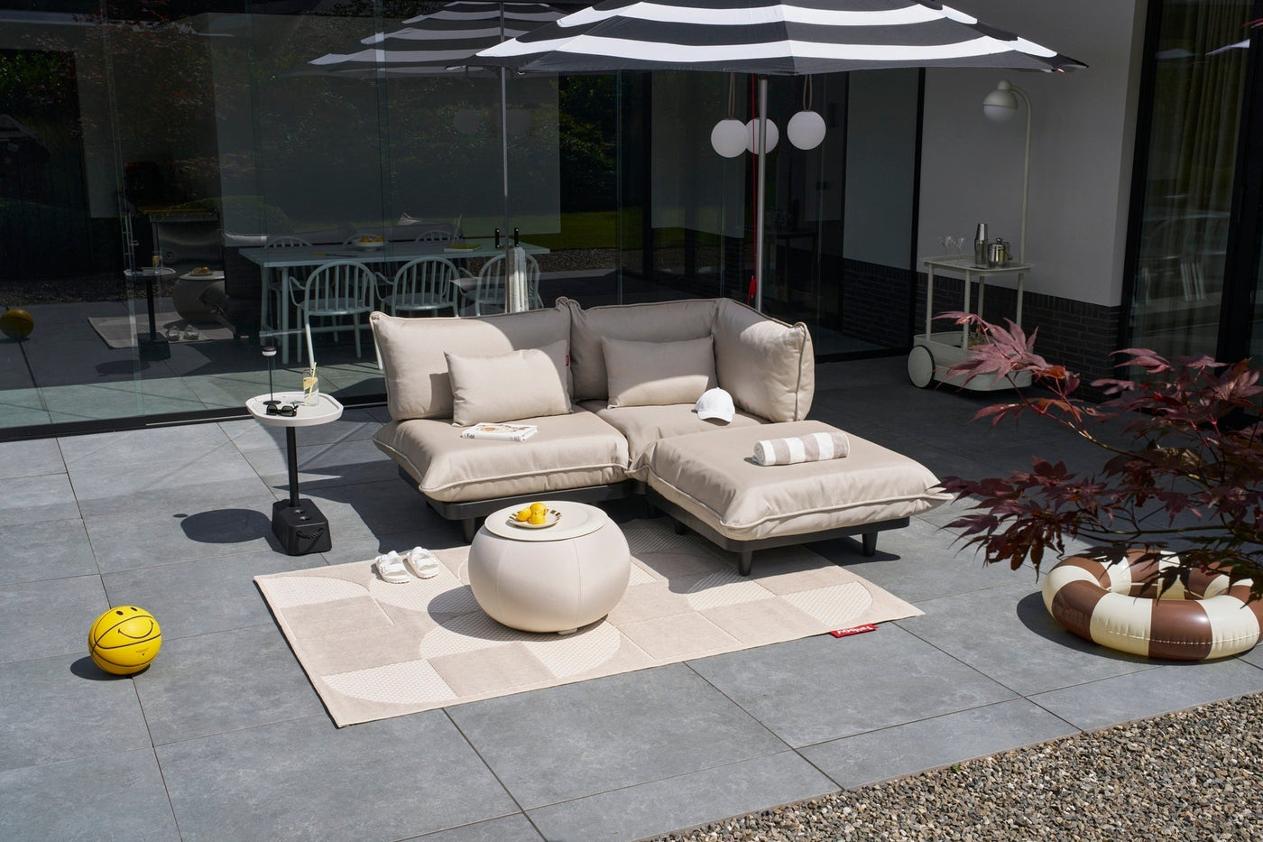 Outdoor setup with beige modular lounge chairs under a striped umbrella on a patio
