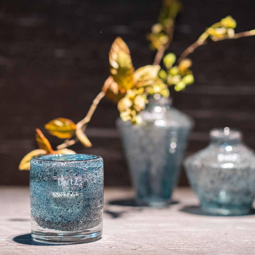 DutZ Galaxy Cylinder in blue, placed on a stone surface with matching decorative glass vases in the background.
