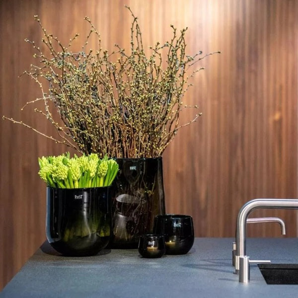 DutZ Pot Candle Holder in smoke, styled on a modern kitchen counter with black vases and fresh green stems.