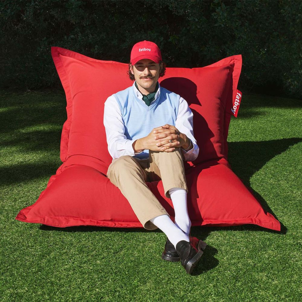 Man relaxing outdoors on a Fatboy Original bean bag in red with a matching Fatboy hat.