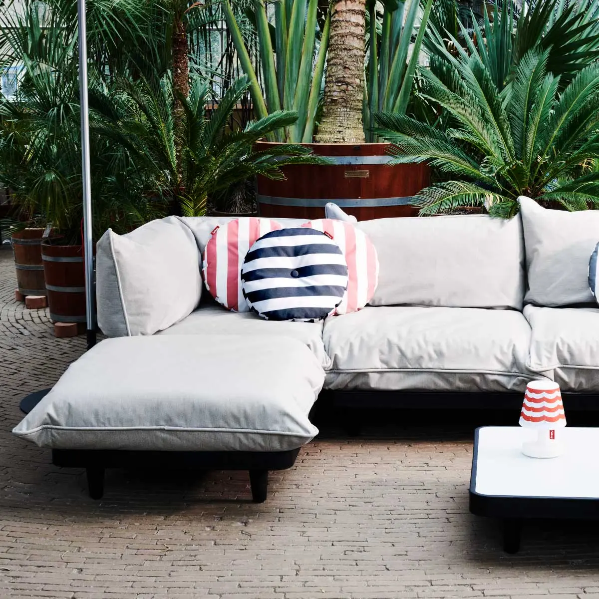 A cosy outdoor lounge area, featuring the Fatboy Paletti corner sofa in mist, matching low table, circle cushions, and Edison the Mini lamp.
