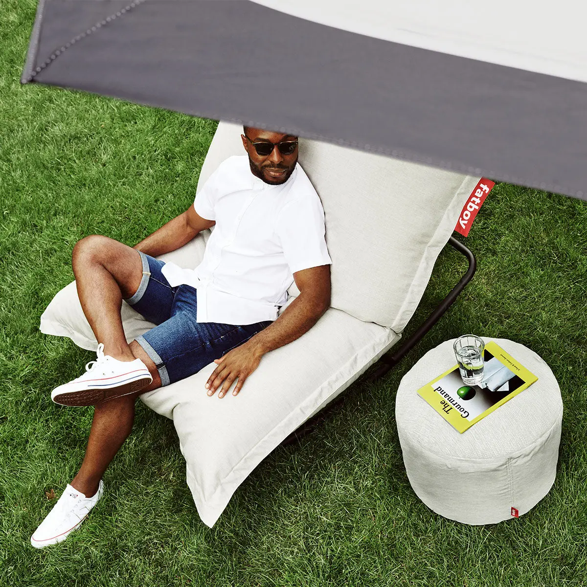 Man lounging outdoors using the Fatboy Original outdoor bean bag on the Rock & Roll rocking chair, and the Point pouf for his essentials.
