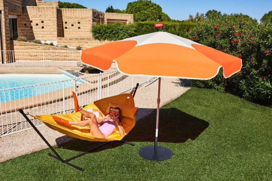 Woman lounging on a Headdemock Hamock under the shade of the Fatboy Sunshady parasol in orange.