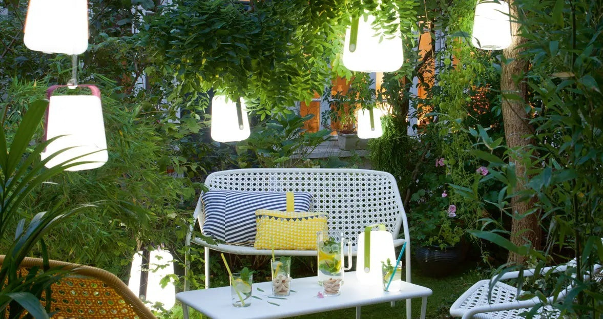 Fermob Balad table lamps and lanterns set up in an outdoor garden. 
