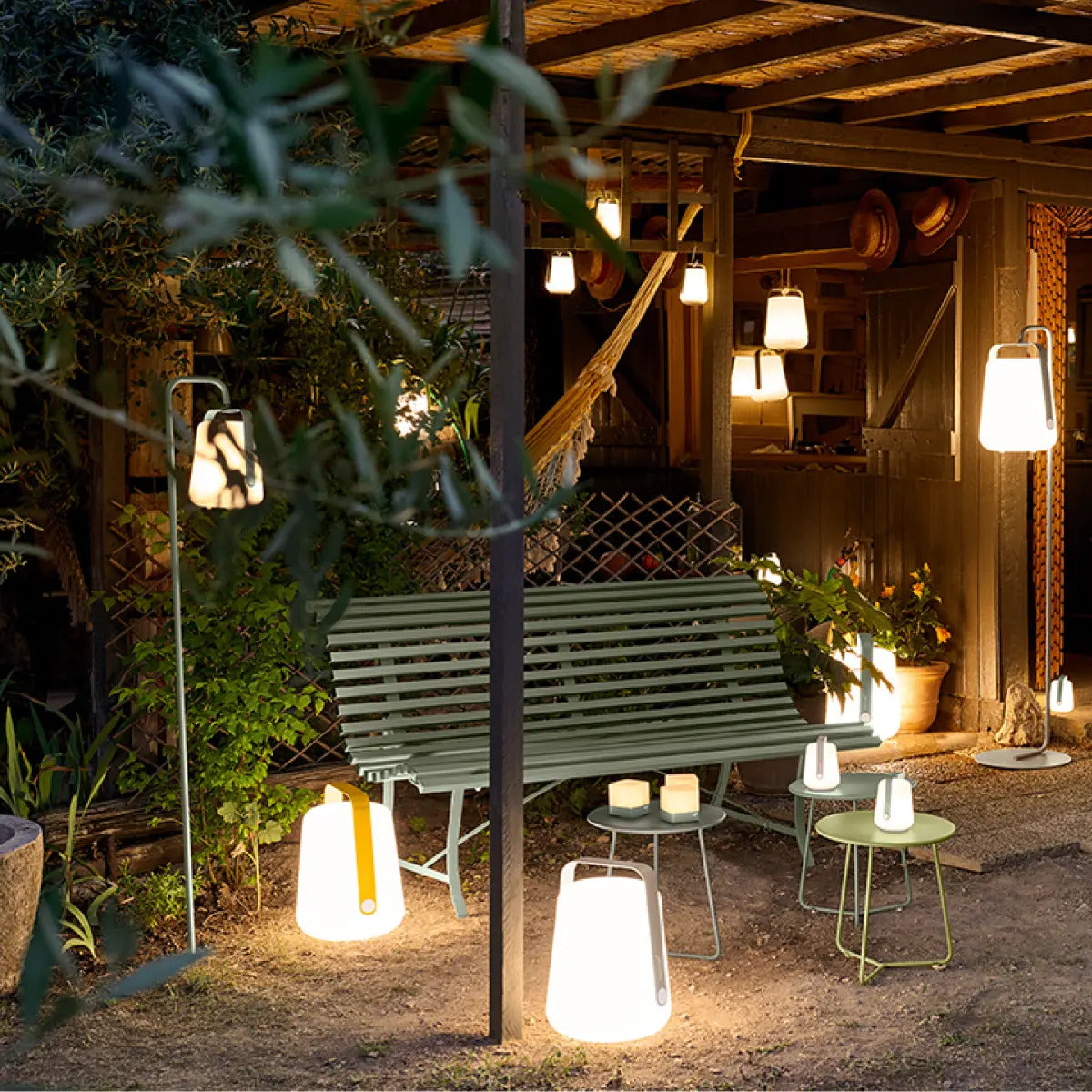 Fermob Louisiane Metal Bench styled as an outdoor bench with a lantern and garden lights.
