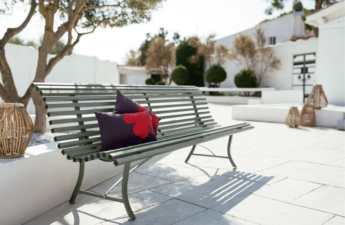 Classic garden bench in green with decorative pillows on a sunny patio.
