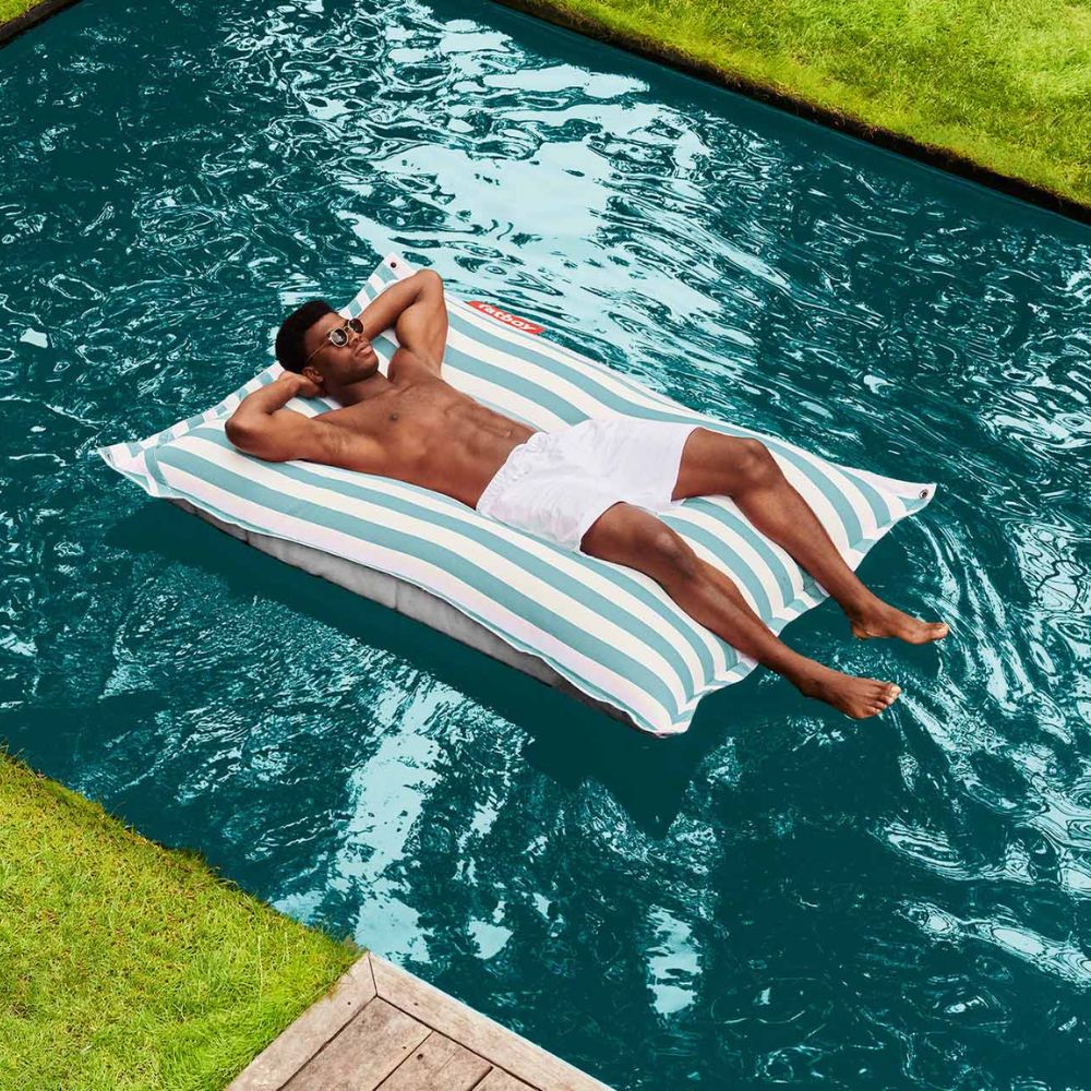 Man lounging on a Fatboy Floatzac Floating Bean Bag in a swimming pool. 