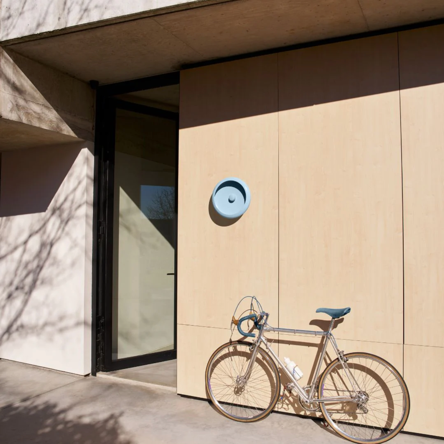 Modern home entrance featuring Fatboy Oloha exterior lamp in blue mounted on the wall with a bicycle, showcasing outdoor lighting and garden lights for stylish outdoor spaces.
