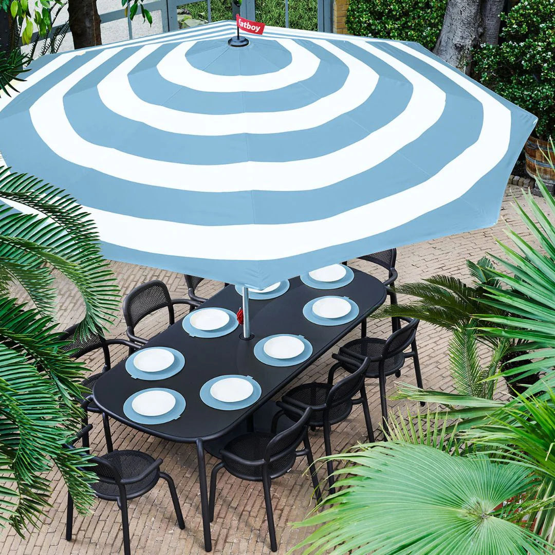 Fatboy Striped Parasol in blue styled with the Toni Tavolo dining table and Toni chairs in an outdoor garden setup.