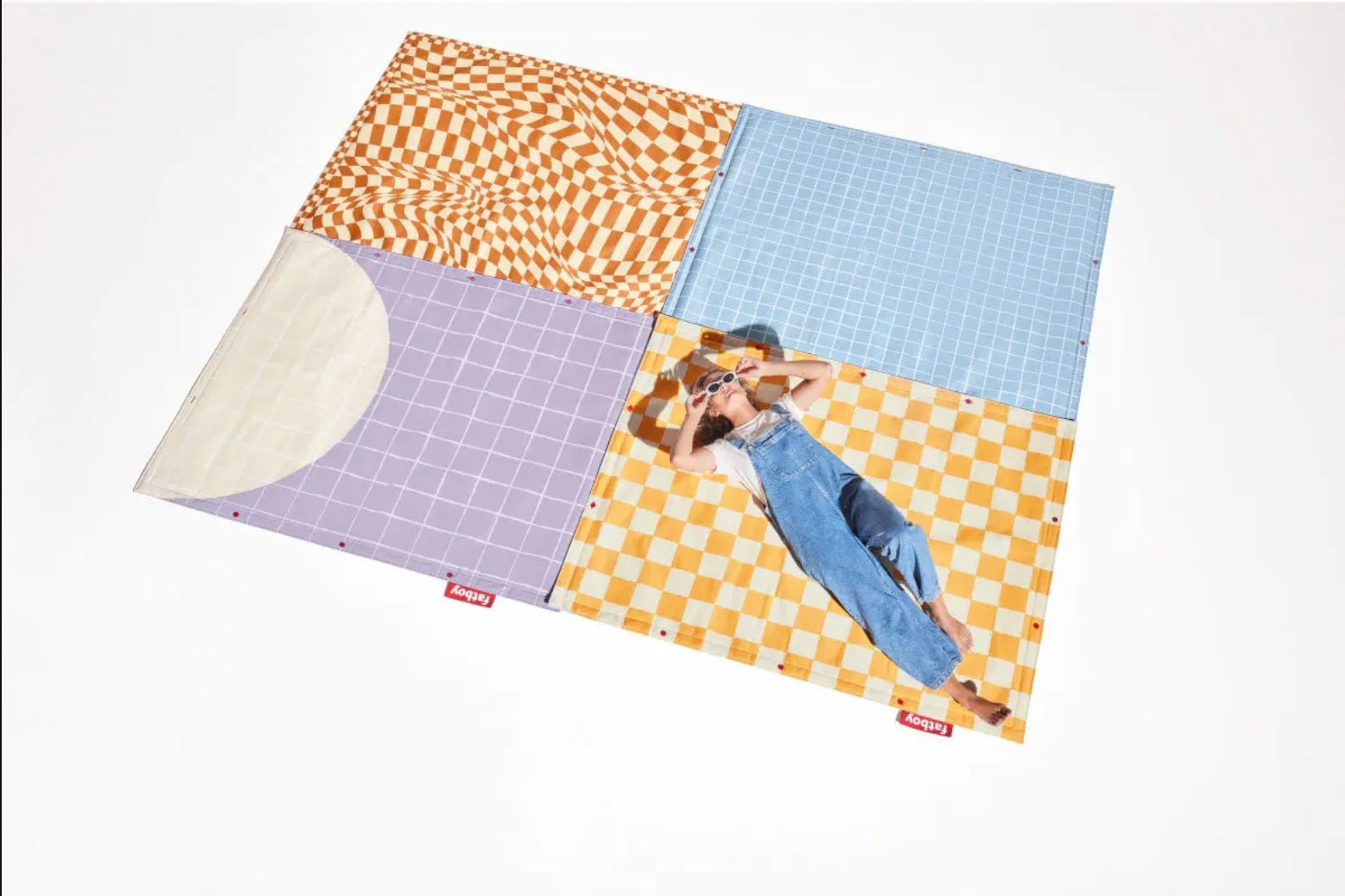 Woman relaxing on Fatboy Flying Carpet outdoor rug with colourful graphic patterns, versatile and durable floor mat for indoor and outdoor spaces